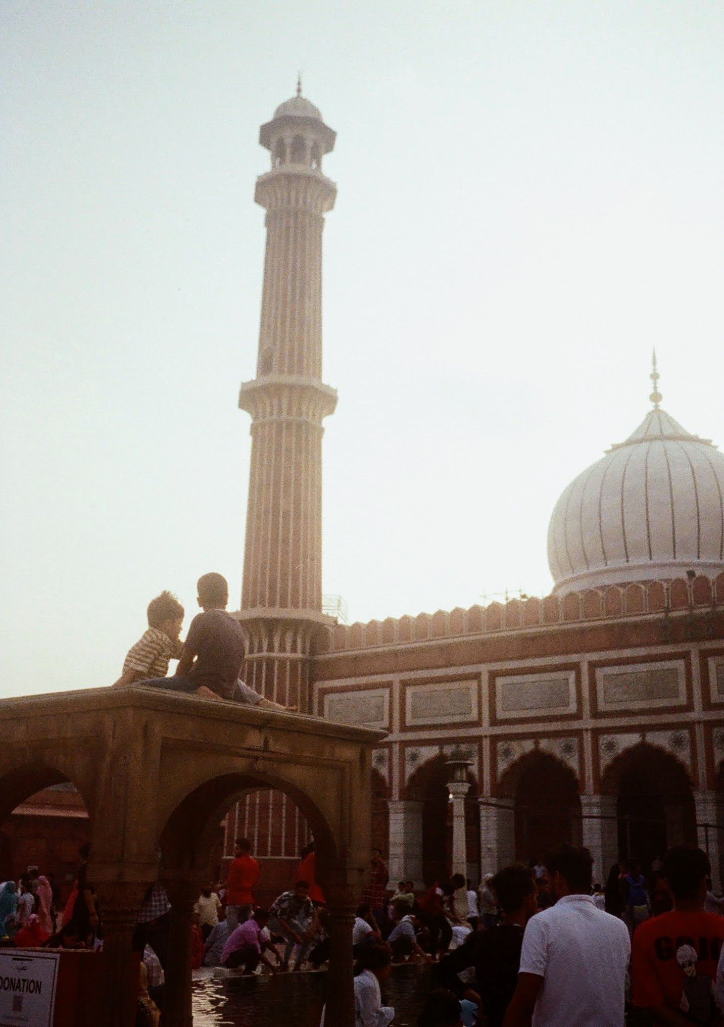 Two children sit atop a small enclosure facing a large mosque dome. 